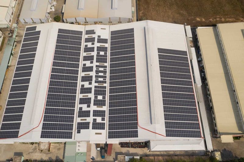 Aerial view of large energy efficient modern factory building with many solar panels neatly installed on white roof
